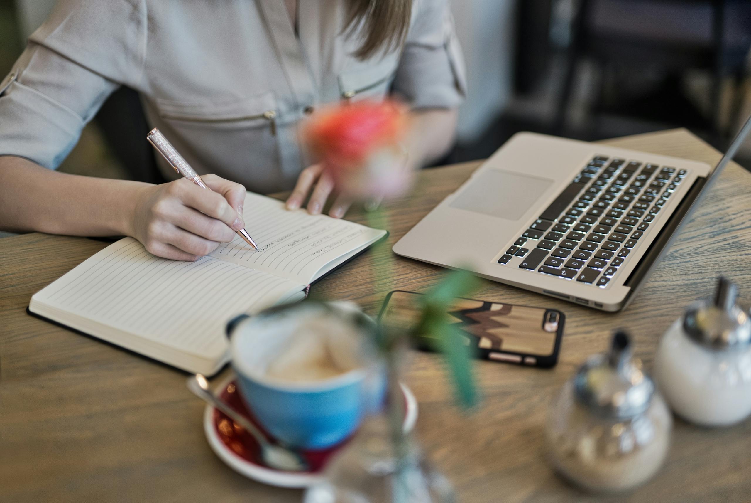 Person Writing On A Notebook Beside Laptop